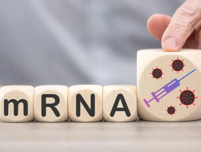 Wooden blocks spelling "mRNA" and a larger fifth block displaying a painted syringe on a table