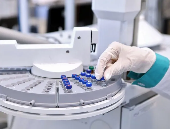 Quality control laboratory tech conducting chromatograph operation. A gloved hand makes an analysis on a gas chromatograph during the development of a new vaccine