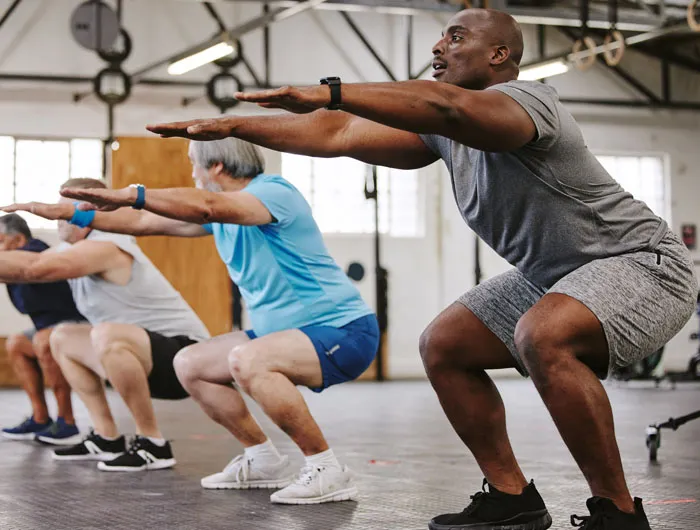 4 older men holding a squat in the gym