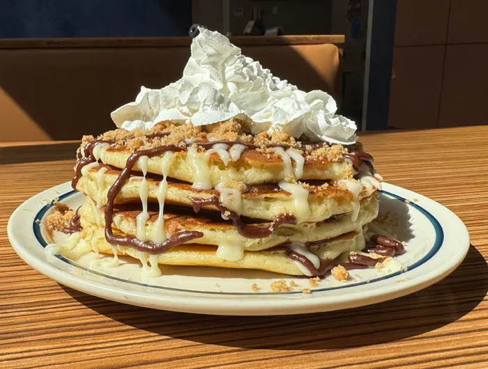 stack of 4 pancakes drizzled with chocolate icing, brown sugar and topped with whipped cream