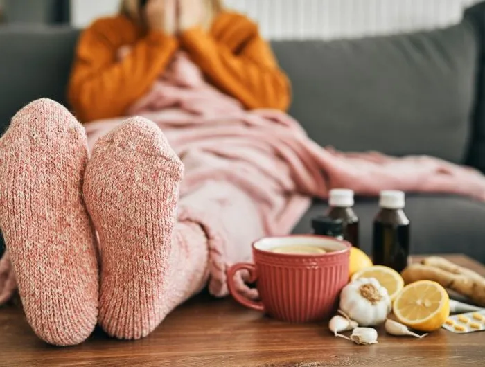 Feet wearing warm socks on a low table beside cold medicine and home remedies