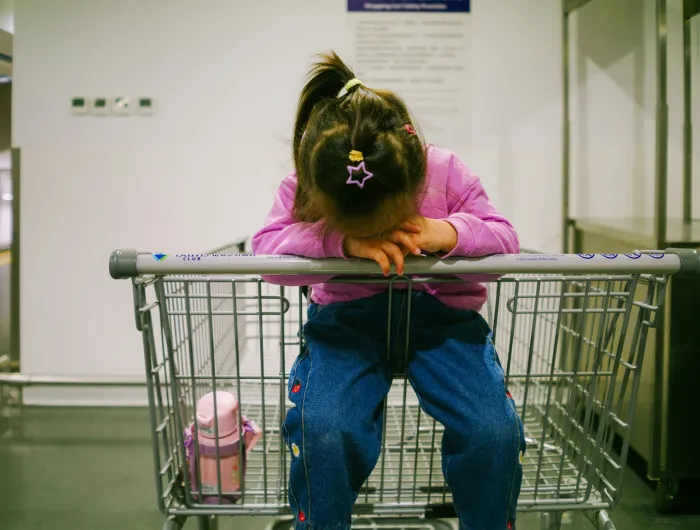 A little girl sitting in an empty shopping cart.