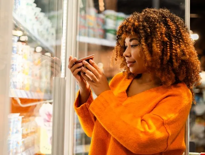 A woman reads the labels of a refrigerated product at the grocery store