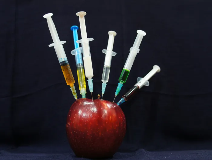 An apple with syringes sticking out of it.