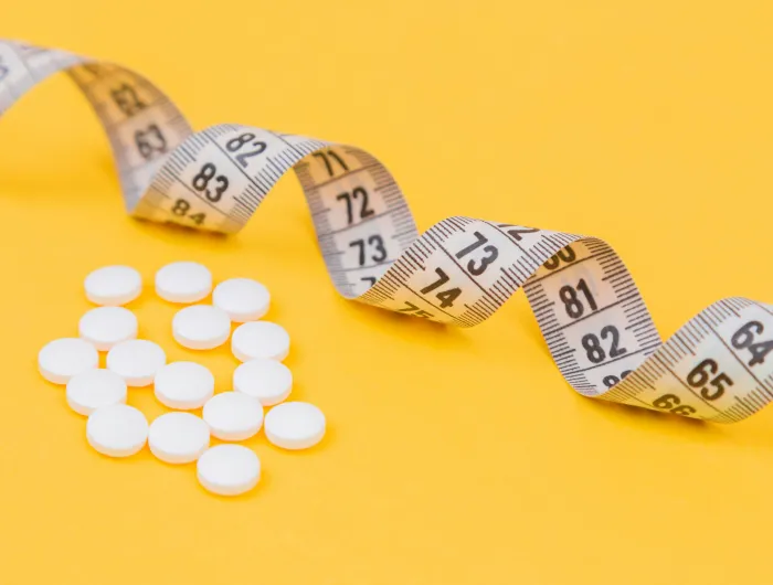 A measuring tape and weight loss pills on a yellow background