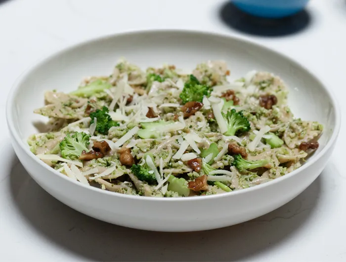 white bowl filled with pesto pasta and walnuts
