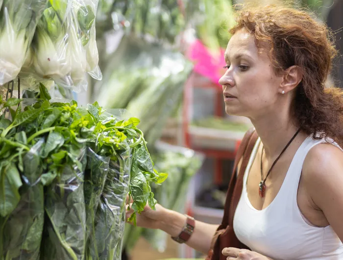 woman choosing a bunch of leafy greens in grocery store