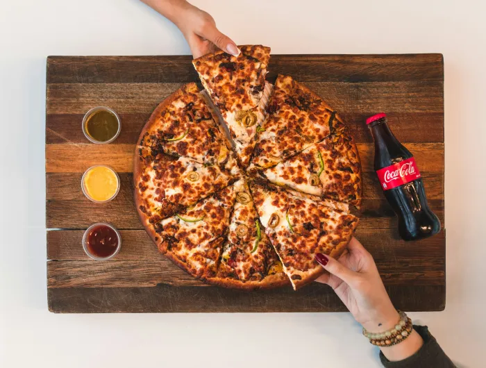 Overhead view of a pizza and bottle of soda on a cutting board