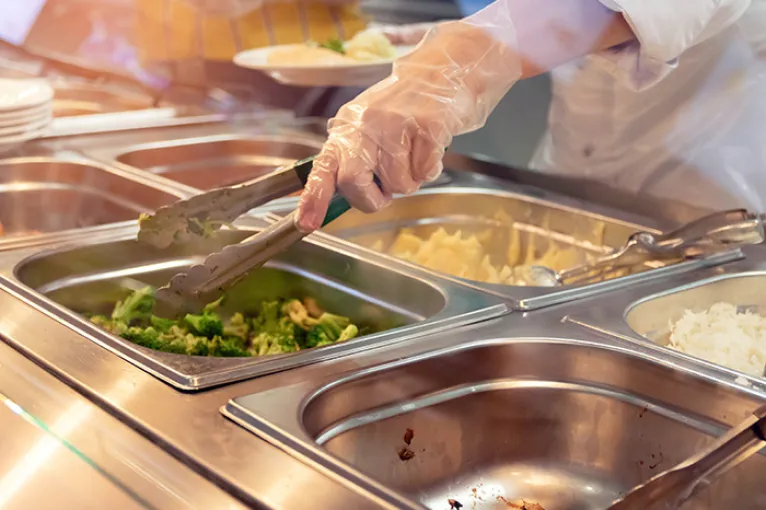 Chef standing behind full lunch service station with assortment of food in trays.