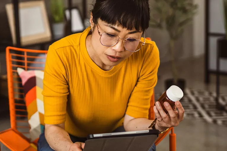 Woman in yellow shirt reading a supplement label and reading on an ipad