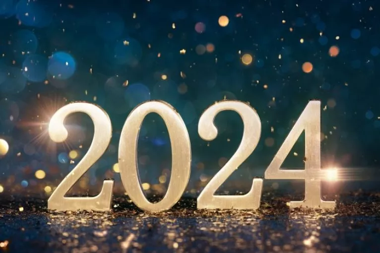 2024 in gold numerals on a reflective surface in front of deep blue bokeh background