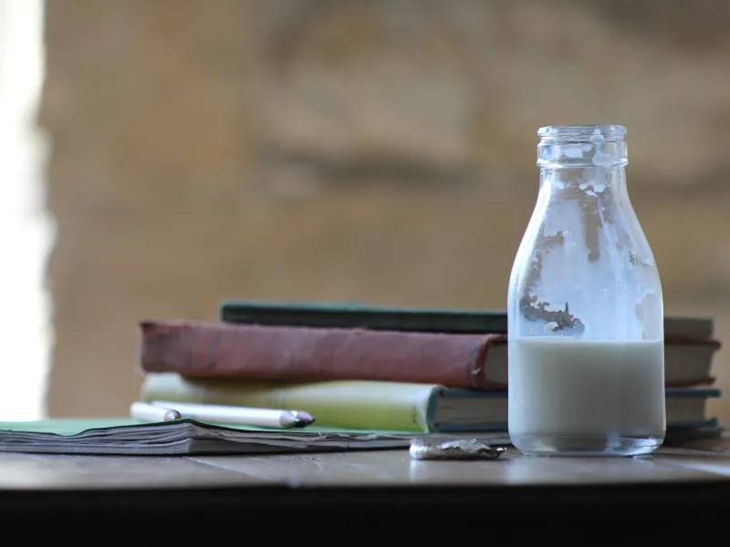 A half-finished bottle of whole milk next to school books