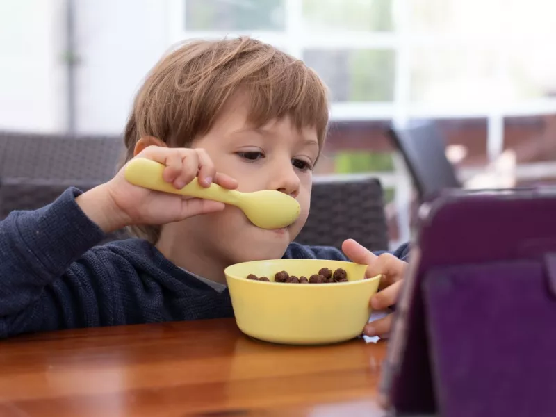 A child watches a show on a tablet while eating cereal