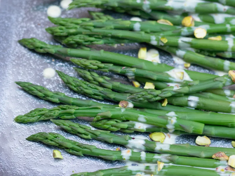 cooked asparagus covered in sauce and pistachios