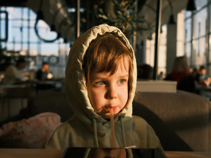 A closeup of a young child wearing a hoodie and drinking from a straw in a restaurant