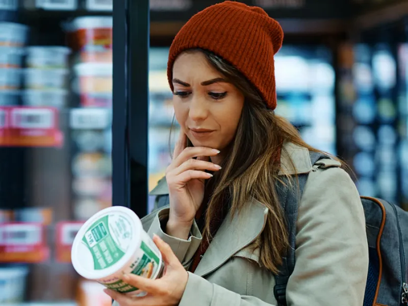 Woman looking confused at back of food container in fridge isle of the grocery store