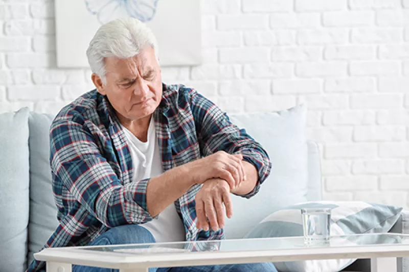 older man sitting on the couch steadying his wrist