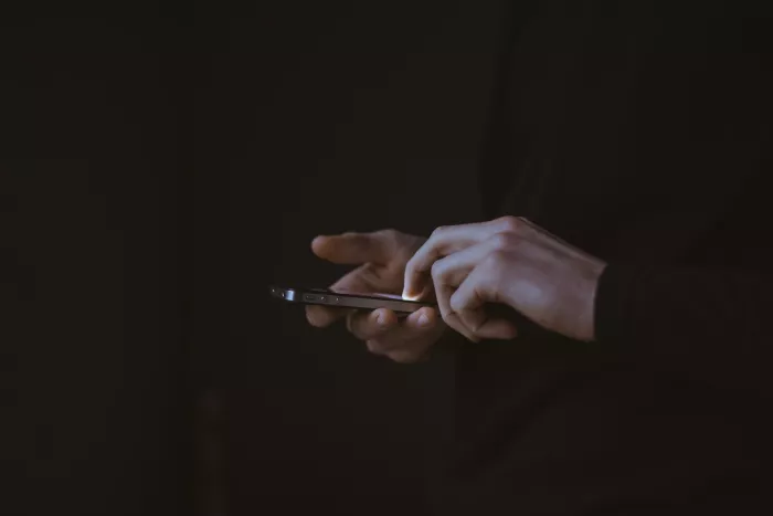 A pair of hands holding an iPhone looms out of an otherwise dark image.