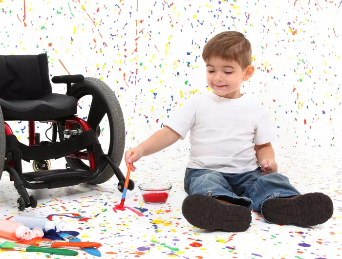 Child sitting on the floor next to wheelchair and playing with paint
