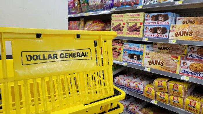 The snack aisle in a Dollar General store, with a branded yellow basket in the foreground and processed foods on the shelves