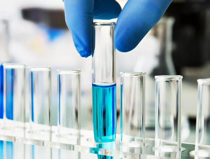 row test tubes one being held by a hand with gloves contains blue liquid