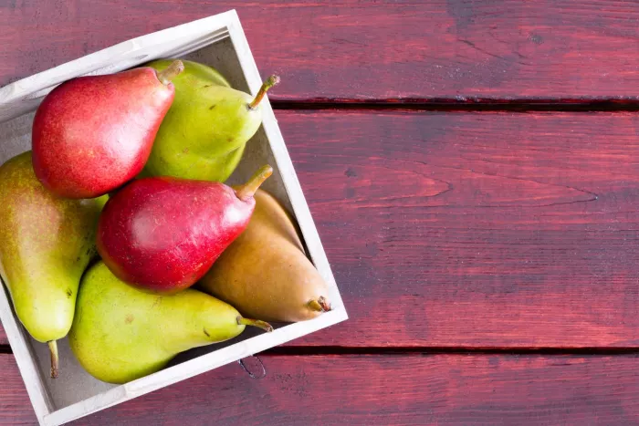 Seasonal produce - flatlay of a variety of fresh pears in a bowl on a wooden table