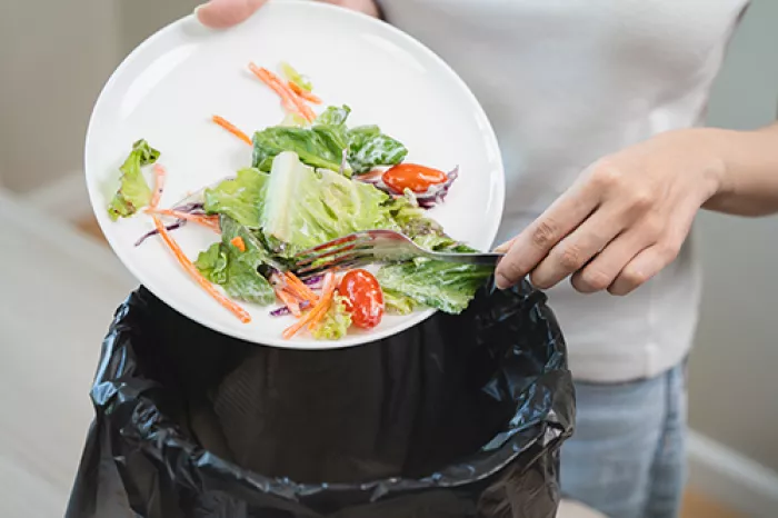 person pushing food off their plate into the trash