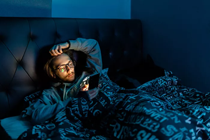 man laying in bed while looking at a bright phone screen in the dark
