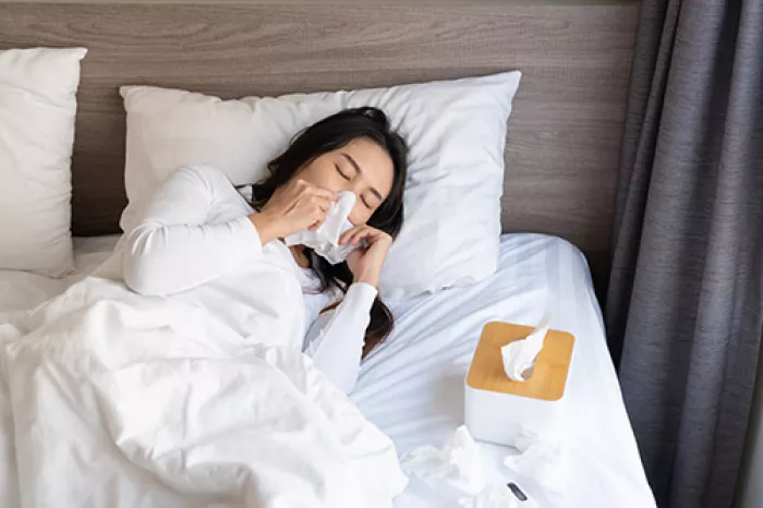 woman laying in bed blowing her nose