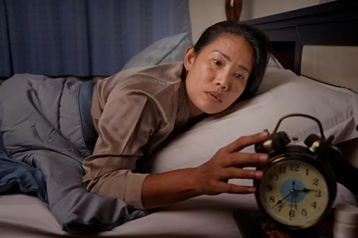 woman turning off alarm while laying in bed