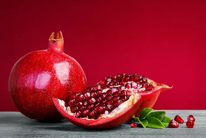 2 pomegranates with one cut open showing seeds with a red background