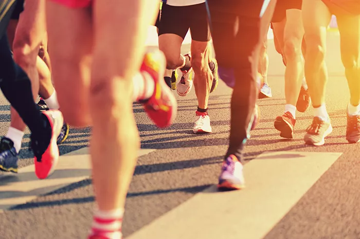 the legs of a large group of runners on pavement in the sunshine