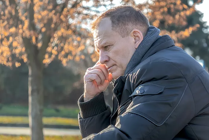 man looking sad while sitting in a park and wearing a black coat