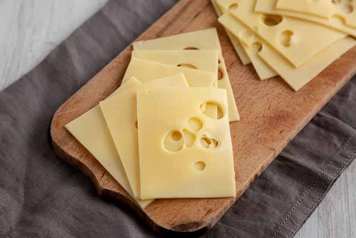 wood cutting board with slices of swiss cheese