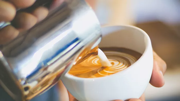 close up of person pouring steamed milk into espresso drink