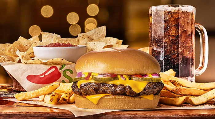 Chilis Big QP burger surrounded by fries with chips and salsa and large soda