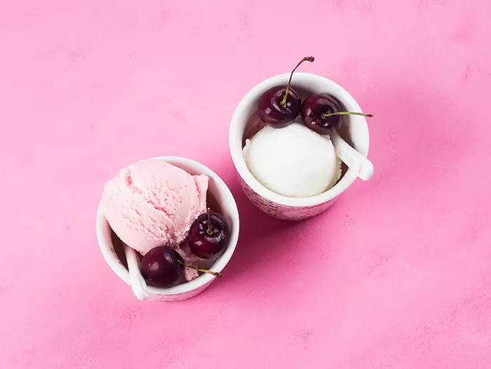 above shot of 2 white ramekins with ice cream and cherries on pink background