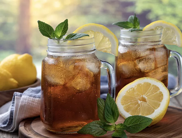 2 glass mugs pf iced tea topped with mint and lemon wedges with lemons around them