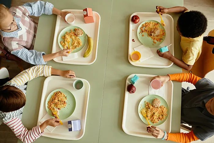 four kids sitting at a table with their lunch trays
