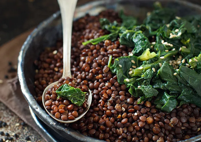wide bowl of black lentils topped with leafy greens