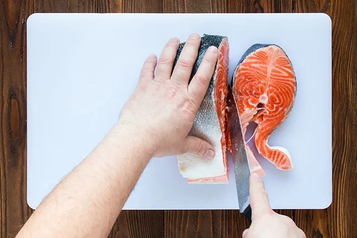 person cutting salmon on a white cutting board