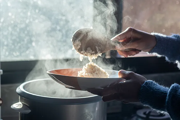 person spooning steaming rice from rice cooker to a bowl