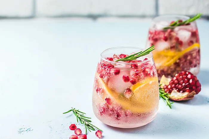 2 clear glasses filled with soda water, pomegranate seeds, lemon slices and sprig of rosemary