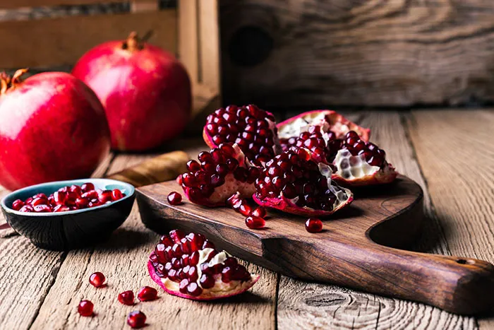 opened pomegranate on cutting board with small bowl filled of seeds