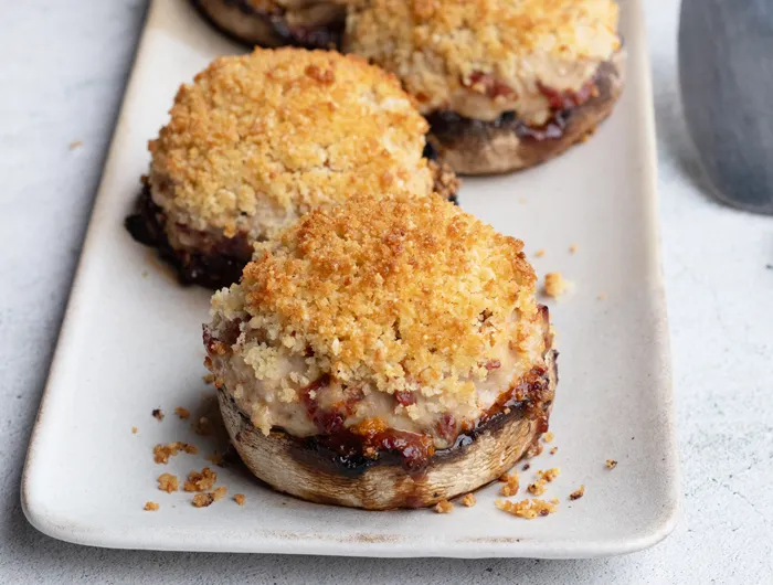 white plate with 2 stuffed Portobello mushrooms topped with breadcrumbs