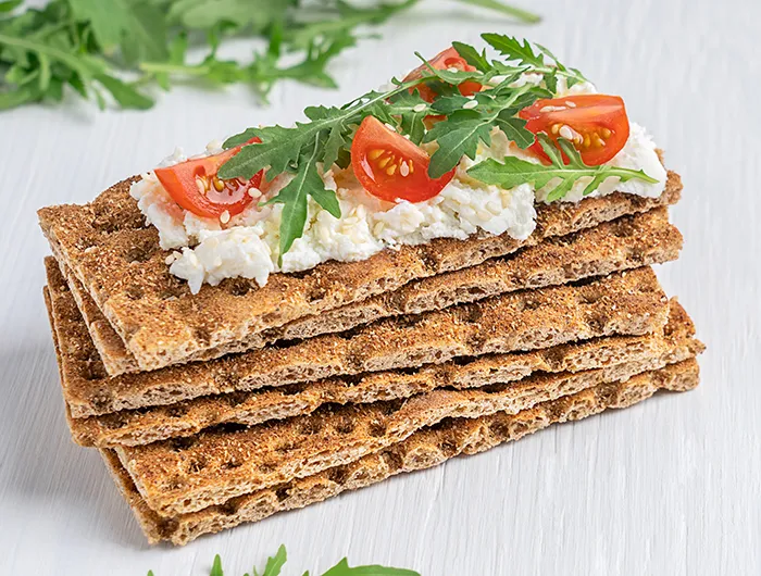 stack of crisp bread. the top one is covered with cheese tomato and arugula 