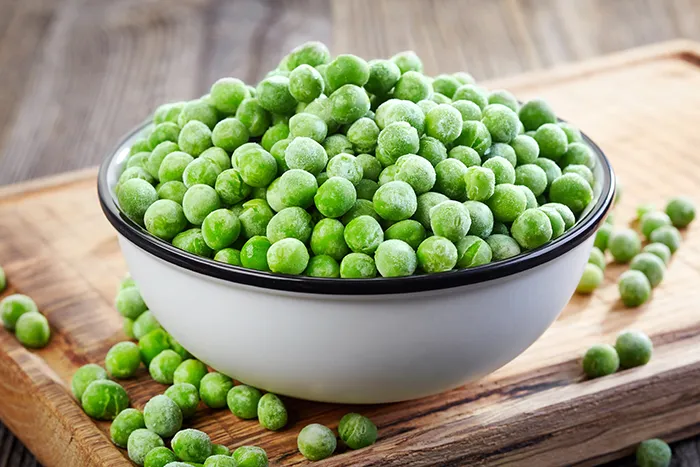 white bowl filled with frozen peas sitting on a wood cutting board