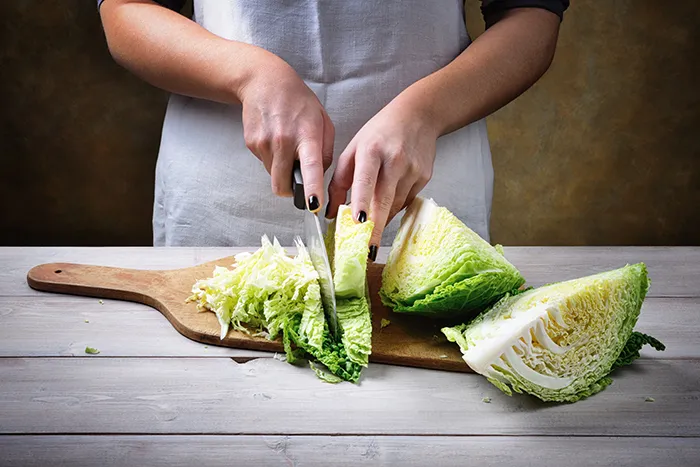 person chopping a head of cabbage on wood cutting board