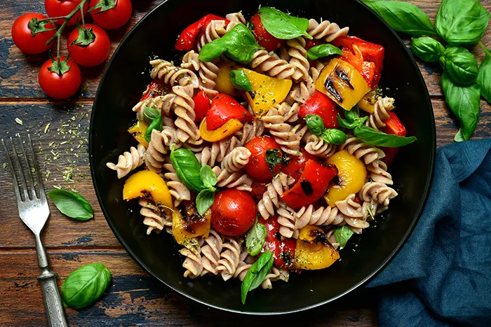 black bowl of whole wheat rotini pasta with peppers, tomatoes and basil mixed in
