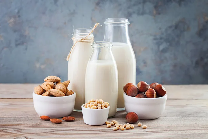 glass jars of milk with bowls of nuts next to them